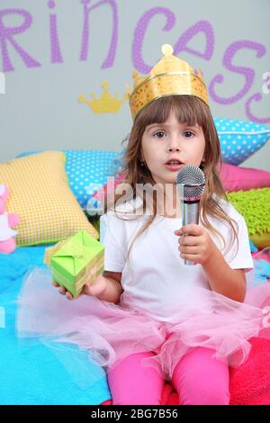 Bambina seduta sul letto con regalo in camera su sfondo grigio parete Foto Stock