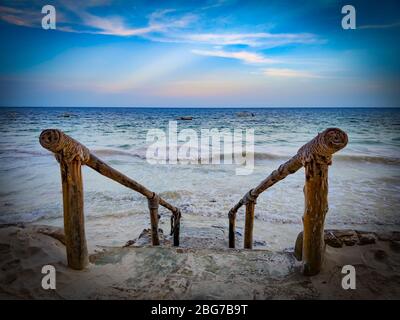 Scale in pietra al mare con ringhiera in legno. Si trova sulla spiaggia di Diani in Kenya, Africa. Onde ad alta marea raggiungono le scale. Foto Stock