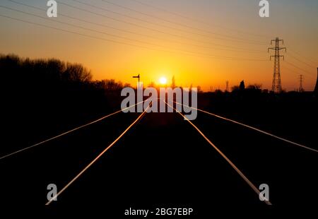 Tramonto sulla linea ferroviaria di trasporto merci di basso livello Warrington che si incline sui binari con un segnale di distanza semaforo Foto Stock