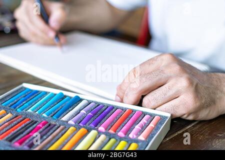 pittura artistica con un gesso pastello di pastello su un foglio bianco di carta e scatola con gessi pastello in colori diversi Foto Stock