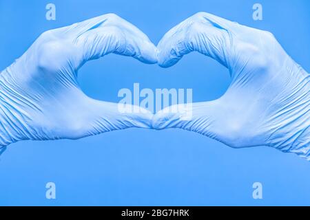 Forma a cuore fatta di mani in guanti per uso medico. Cuore fatto di guanti medici su sfondo blu. Forma a cuore fatta con le mani. Amore, positività, emozione Foto Stock