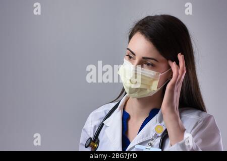 Maschera di regolazione per operatore sanitario femminile. Lavorare con pazienti di Coronavirus in DPI giallo su sfondo grigio Foto Stock