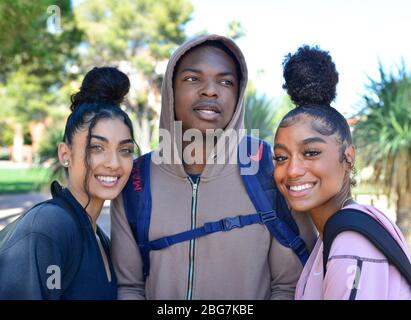 Belle giovani donne e uomo di colore, godere della vita del campus come studenti con felpa e capelli alla moda updo e sorrisi in Arizona, Stati Uniti, Foto Stock