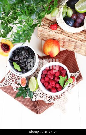 Lamponi e mora in ciotole piccole su tovagliolo su tavolo di legno Foto Stock