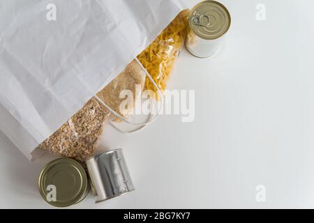 Vari alimenti in scatola, pasta, riso e cereali crudi su un tavolo in sacchetto di carta con spazio per copia Foto Stock