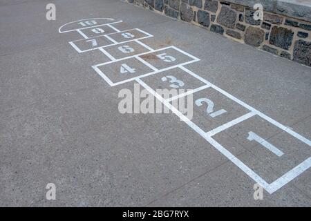 gioco di bambina hop-scotch sul cortile della scuola asfaltato linee e numeri dipinti Foto Stock