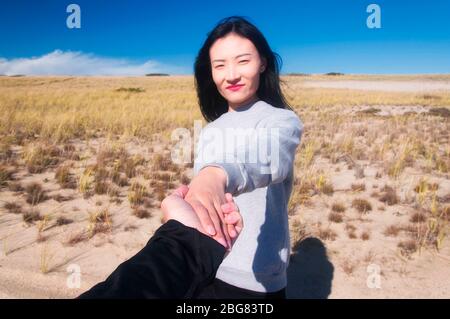 Una donna cinese che tiene le mani con un punto di fuoco uomo sulle mani con il viso sfocato sulla zona panoramica nazionale della riva del mare a Cape Cod, Massachus Foto Stock