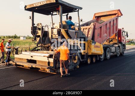 lavoratori edili che utilizzano una macchina per pavimentazione che posa uno strato fresco di asfalto durante la costruzione di autostrade Foto Stock