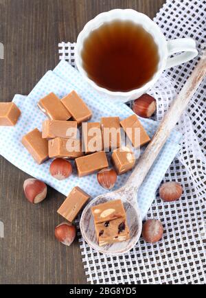 Molti toffee in cucchiaio e tazza di tè su tovaglioli su tavola di legno Foto Stock