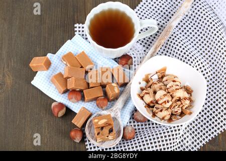 Molti toffee in cucchiaio e tazza di tè su tovaglioli su tavola di legno Foto Stock