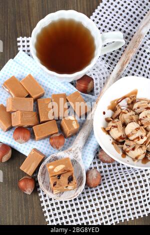 Molti toffee in cucchiaio e tazza di tè su tovaglioli su tavola di legno Foto Stock