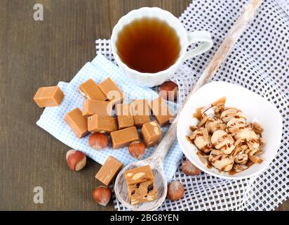 Molti toffee in cucchiaio e tazza di tè su tovaglioli su tavola di legno Foto Stock