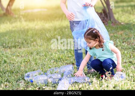 Carino bambine pulizia lettiera in plastica sull'erba. Bambini I volontari la pulizia di lettiera e mettere la bottiglia di plastica nel sacchetto di riciclaggio. Giornata mondiale dell'ambiente. Foto Stock