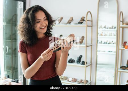 donna asiatica shopping scarpe in boutique. cliente che guarda il prezzo del prodotto Foto Stock