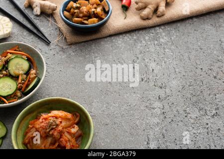 fuoco selettivo di ciotole con kimchi vicino a bacchette e zenzero su superficie di cemento Foto Stock