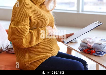 Bella giovane donna incinta che fa lista delle cose necessarie a casa Foto Stock