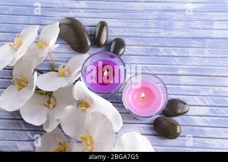Belle candele colorate, pietre spa e fiori di orchidee, su sfondo di legno colore Foto Stock
