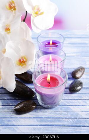 Belle candele colorate, pietre spa e fiori di orchidee, su tavolo di legno colore, su sfondo chiaro Foto Stock