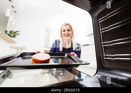 Ritratto di una giovane donna che prepara il cibo in cucina. La giovane casalinga sta tenendo la carne appena sfornata Foto Stock