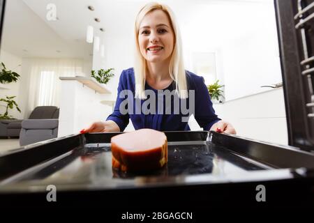 Ritratto di una giovane donna che prepara il cibo in cucina. La giovane casalinga sta tenendo la carne appena sfornata Foto Stock