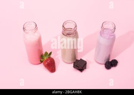Vista ad angolo alto di bottiglie di milkshake con fragola, more e pezzi di cioccolato su sfondo rosa Foto Stock