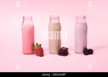 Bottiglie di milkshake con fragola, more e pezzi di cioccolato su sfondo rosa Foto Stock