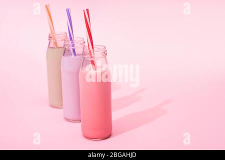 Bottiglie di frullati di fragole, fragole e cioccolato con cannucce da bere su sfondo rosa Foto Stock