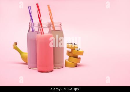 Bottiglie di frittelle di fragole e cioccolato con cannucce e banana tagliata con scaglie di cioccolato su sfondo rosa Foto Stock