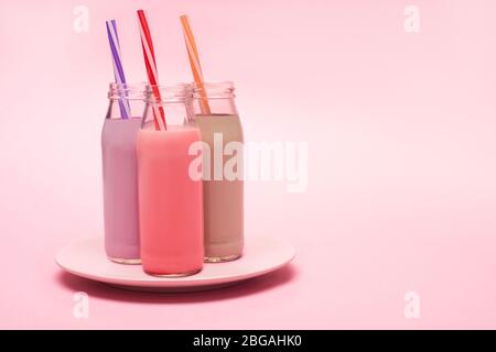 Bottiglie di frittelle di fragole, fragole e cioccolato con cannucce da bere su piatto su fondo rosa Foto Stock