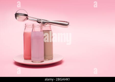 Bottiglie di milkshake di fragola, fragola e cioccolato con paletta su piatto su fondo rosa Foto Stock