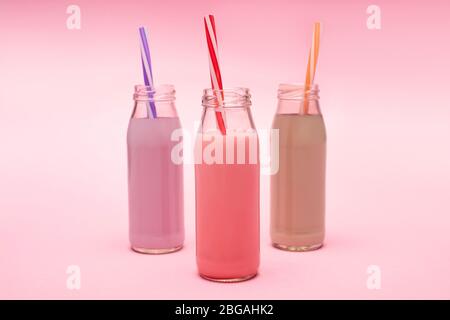 Bottiglie di frittelle di fragole, fragole e cioccolato colorate con cannucce da bere su rosa Foto Stock