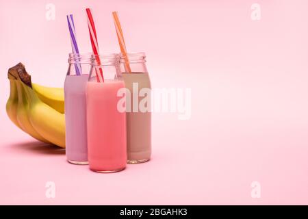 Bottiglie di fragole, fragole e cioccolato con cannucce vicino alle banane su sfondo rosa Foto Stock