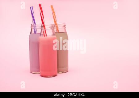 Bottiglie di frittelle di fragole, fragole e cioccolato con cannucce da bere su sfondo rosa Foto Stock