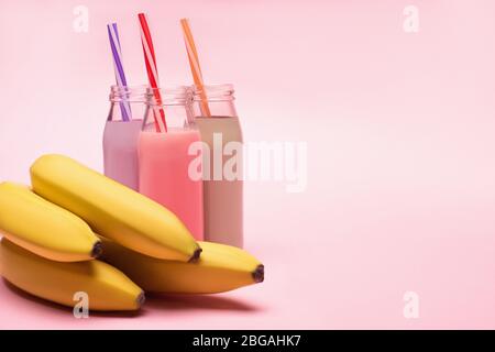 Bottiglie di frittelle di fragole e cioccolato con cannucce e banane su sfondo rosa Foto Stock