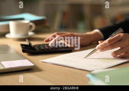 Primo piano di donna imprenditore mani controllo del documento utilizzando la calcolatrice di notte Foto Stock