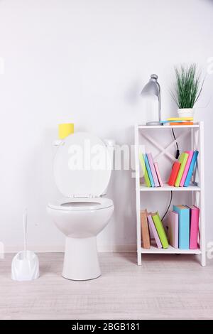 WC bianco e stativo con libri, su sfondo a parete a colori Foto Stock