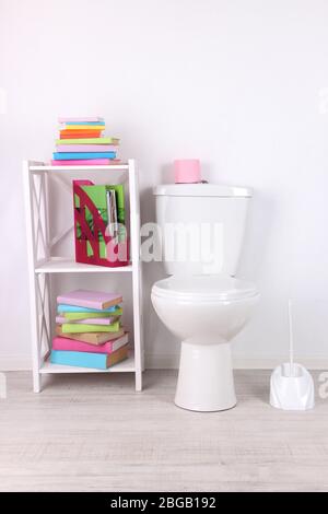 WC bianco e stativo con libri, su sfondo a parete a colori Foto Stock