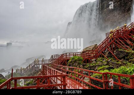 Cascate del Niagara, NY, USA - 13 giugno 2019: I visitatori in impermeabili su scale di legno bagnate fanno un tour sotto gli schizzi delle cascate americane Foto Stock