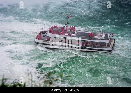 Cascate del Niagara, NY, USA - 13 giugno 2019: Nave con turisti si sposta alle cascate del Niagara, l'esperienza del tour in barca delle cascate è l'attrazione più antica del Nord America, e. Foto Stock