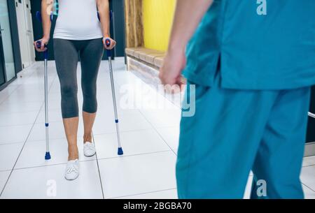 Paziente donna che utilizza stampelle per la riabilitazione dopo lesioni. Fisioterapista che assiste un paziente. Foto Stock