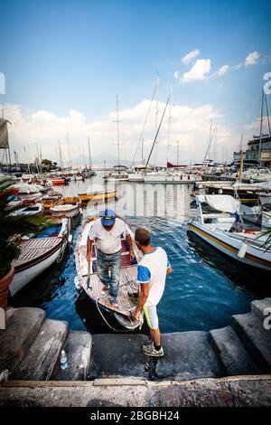 Napoli, Italia. 09 agosto 2015: Antica città portuale. Due pescatori stanno scendendo dalla loro piccola barca nel porto di Napoli. Molte altre barche e dee Foto Stock