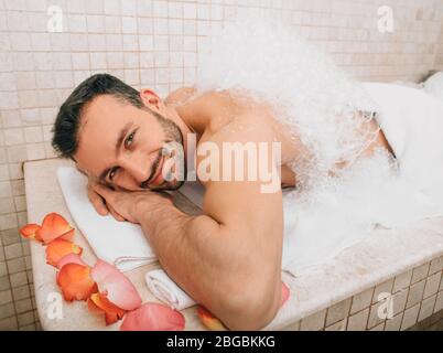 Uomo orientale che guarda nella cornice durante un massaggio schiumoso in un hammam . Bagno turco tradizionale Foto Stock