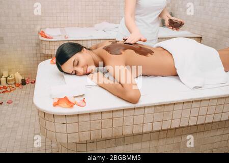 Bella donna che gode procedura di confezionamento del cioccolato. La procedura della maschera corpo al cioccolato nutre la pelle con vitamine, minerali e antidepressivi Foto Stock