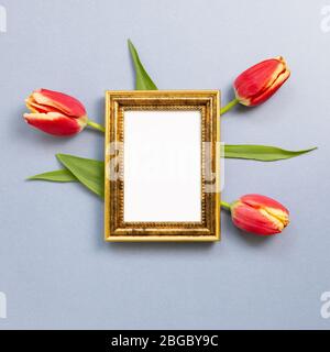 Cornice fotografica vuota con fiori tulipano rossi su sfondo grigio blu. Composizione floreale, piatto, vista dall'alto, spazio per copie Foto Stock