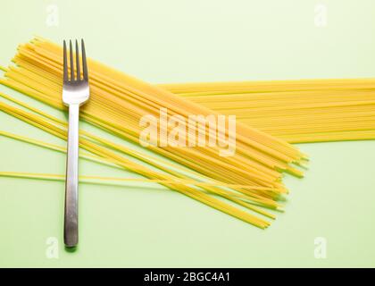Composizione creativa, due grappoli di spaghetti crudi appoggiati su sfondo verde, una forchetta appoggiata sul lato sinistro della cornice. Foto Stock