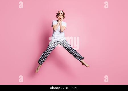 Foto a lunghezza intera di divertente signora salto alto mani su guance aperta bocca indossare abiti da sonno maschera bianco t-shirt pajama pantaloni a piedi nudi isolato Foto Stock