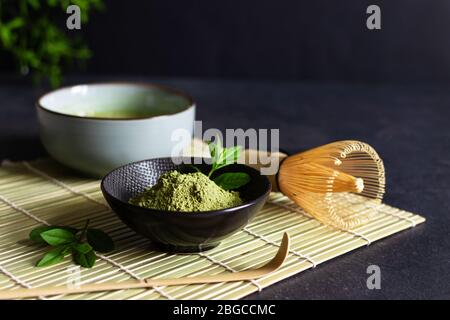 Tè e tè matcha verde biologico su tappetino giapponese su sfondo nero. Cerimonia del tè giapponese. Cucchiaio Chashaku e whis di bambù chasen Foto Stock