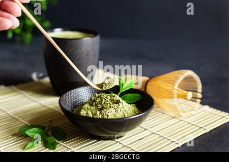 Tè e tè matcha verde biologico su tappetino giapponese su sfondo nero. Cerimonia del tè giapponese. Cucchiaio Chashaku e whis di bambù chasen Foto Stock
