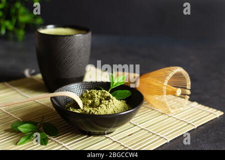 Tè e tè matcha verde biologico su tappetino giapponese su sfondo nero. Cerimonia del tè giapponese. Cucchiaio Chashaku e whis di bambù chasen Foto Stock