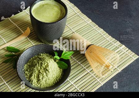 Tè e tè matcha verde biologico su tappetino giapponese su sfondo nero. Cerimonia del tè giapponese. Cucchiaio Chashaku e whis di bambù chasen Foto Stock